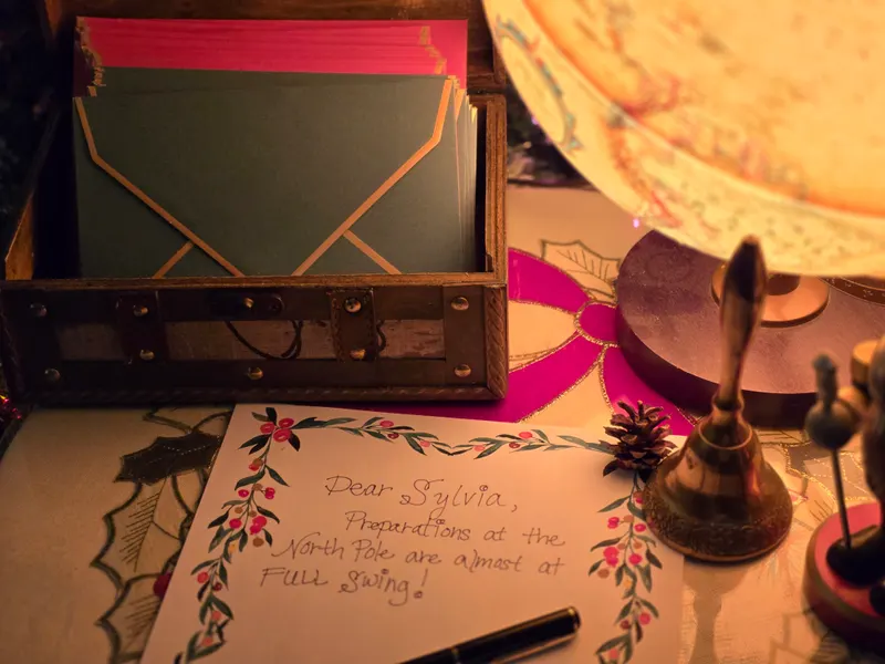 A letter on berry stationery beside a brass bell, a pen and a chest of envelopes